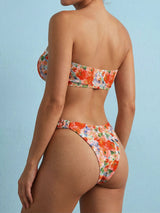 Back view of a woman wearing an orange and pink floral print strapless bikini.