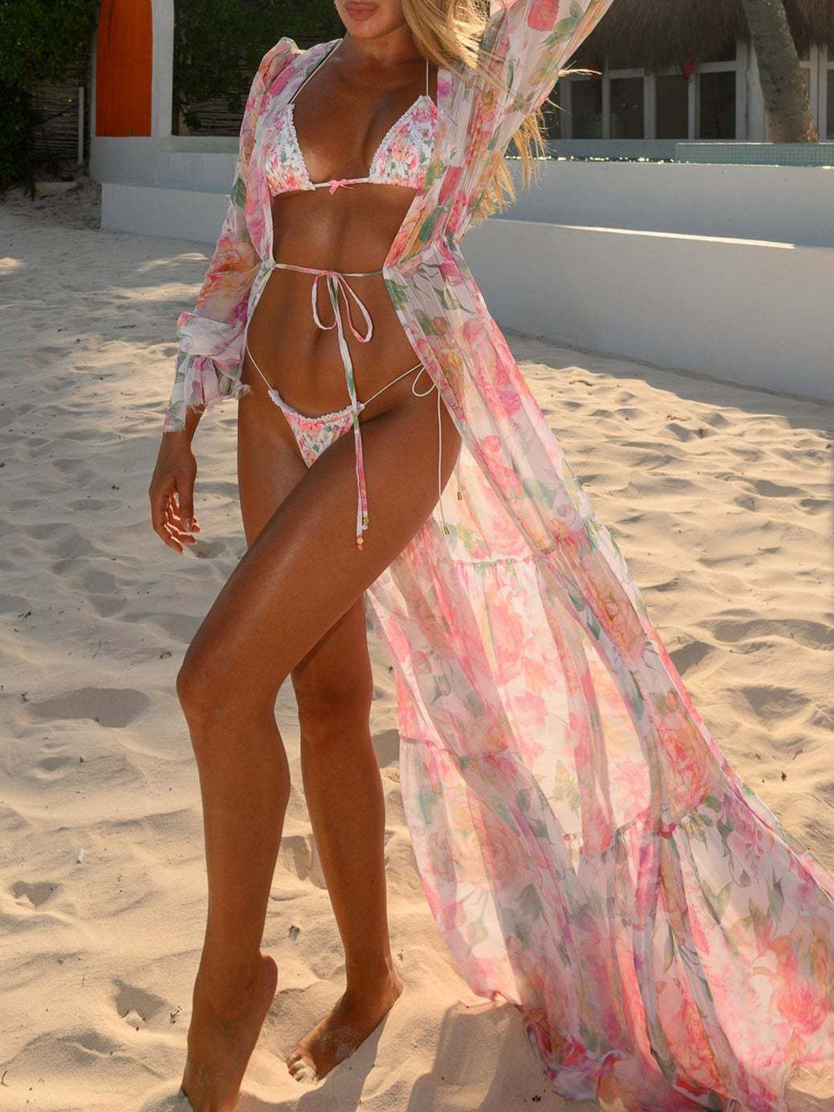 Woman in a floral bikini and a sheer pink floral duster on a sandy beach.