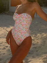 A woman in a floral print strapless swimsuit on a sandy beach.