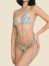 Woman wearing a white, teal, and blue patterned bikini with triangle cups and tie-side bottoms, front view.