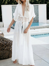 Woman wearing a white sheer maxi dress with lace trim and a tie front, standing by a pool.