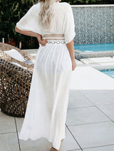 Back view of a woman wearing a white sheer maxi dress with lace trim, standing by a pool.