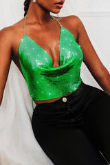 Woman wearing a green metallic mesh halter top with a plunging neckline and black pants, front view.