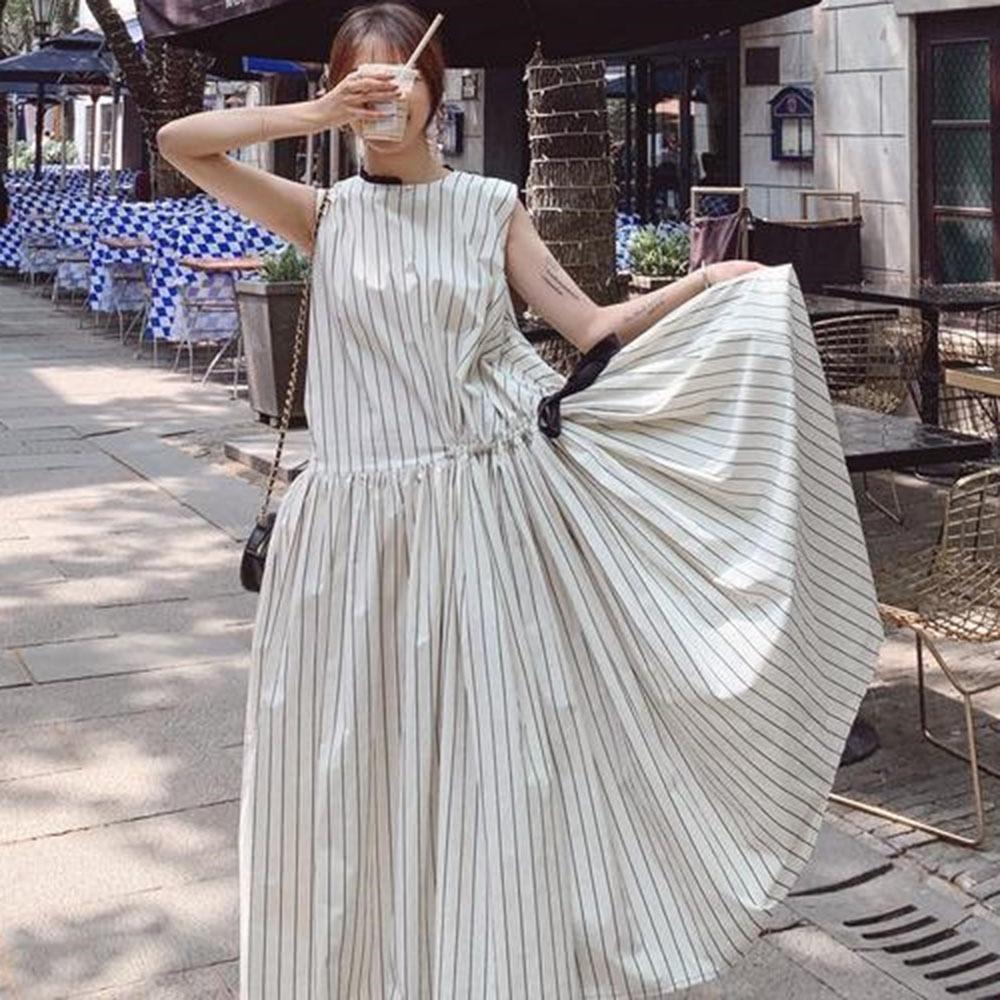 Woman wearing a long white sleeveless dress with black vertical stripes, lifting the skirt to show the fullness, holding a drink.