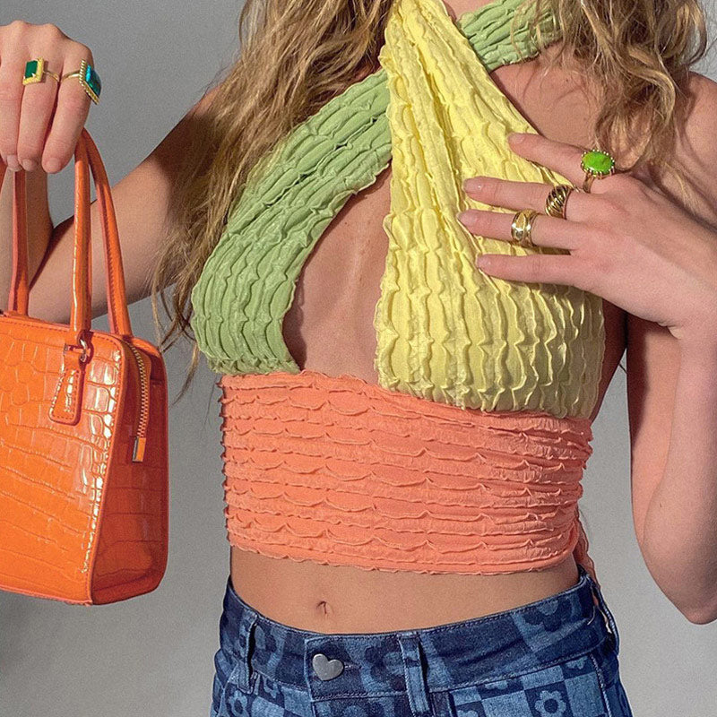 Close-up of a woman wearing a multi-colored halter top, holding an orange handbag and showing off her rings.