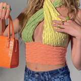 Close-up of a woman wearing a multi-colored halter top, holding an orange handbag and showing off her rings.