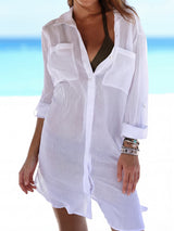 Woman wearing a white sheer button-down cover-up over a bikini top, standing on a beach.