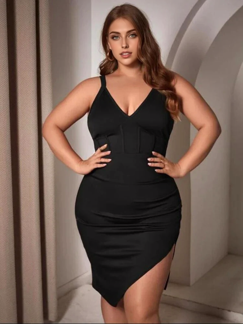 A plus-size woman in a black V-neck, spaghetti strap dress with a corset detail and an asymmetrical hem with a thigh slit.