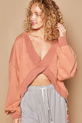 Woman wearing a peach cropped sweatshirt with a cross-over v-neck and gray sweatpants.