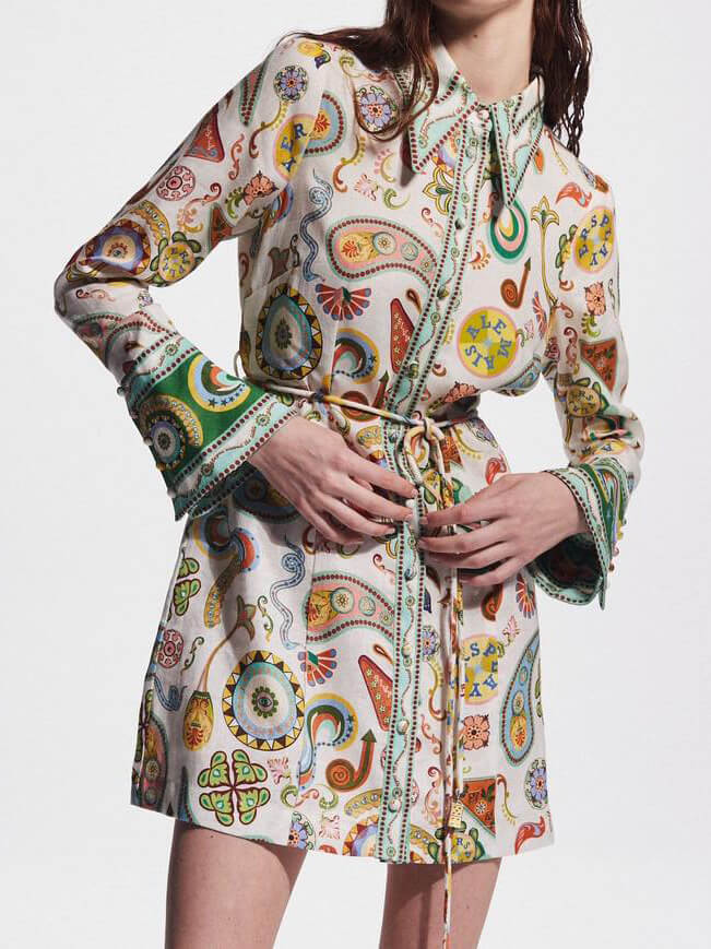 Close-up of a woman adjusting the belt on a colorful paisley print shirt dress.