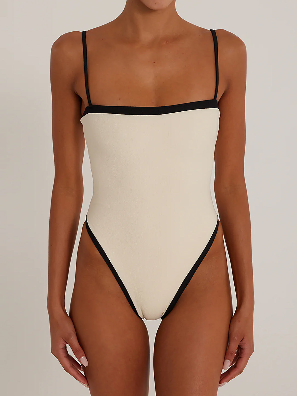 Woman wearing a cream one-piece swimsuit with black trim