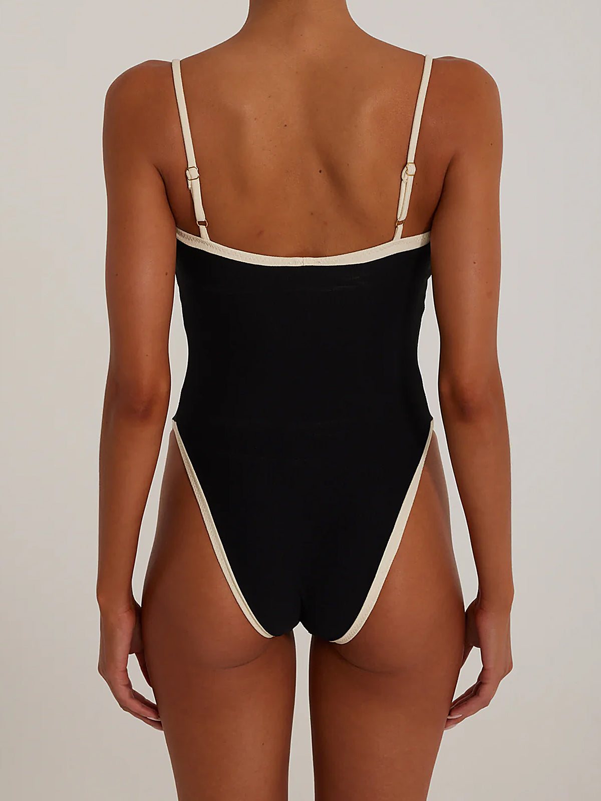Back view of a woman in a black one-piece swimsuit with white trim