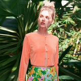 Woman with her hair in a bun wearing a peach cropped cardigan and floral pants in a tropical setting.