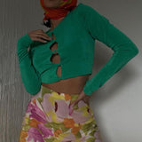 Woman in a green cropped long-sleeve top and a floral skirt, with a colorful headscarf.