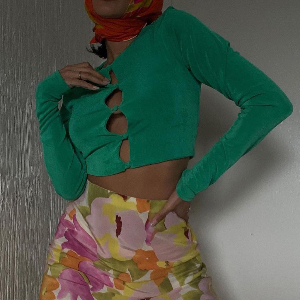 Woman in a green cropped long-sleeve top and a floral skirt, with a colorful headscarf.
