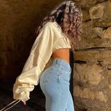 Back view of a woman in a cream cropped shirt and light blue jeans, showing the voluminous sleeves.
