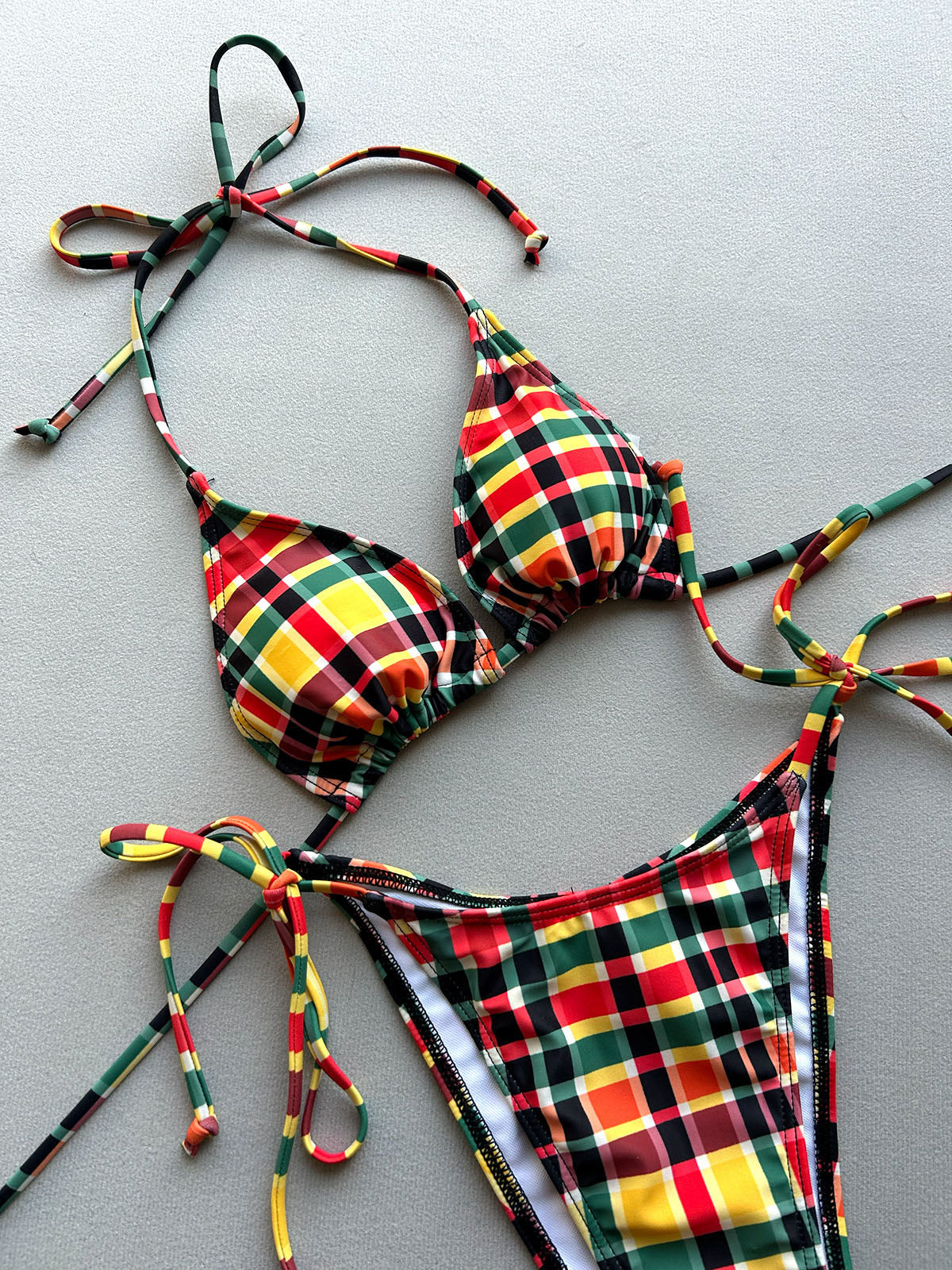 A red, green, yellow, and brown plaid triangle bikini top and string bikini bottom laid flat.