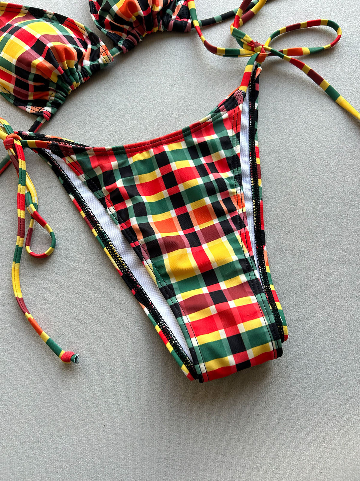 Close-up of the red, green, yellow, and brown plaid string bikini bottom, showing the tie closure and white lining.
