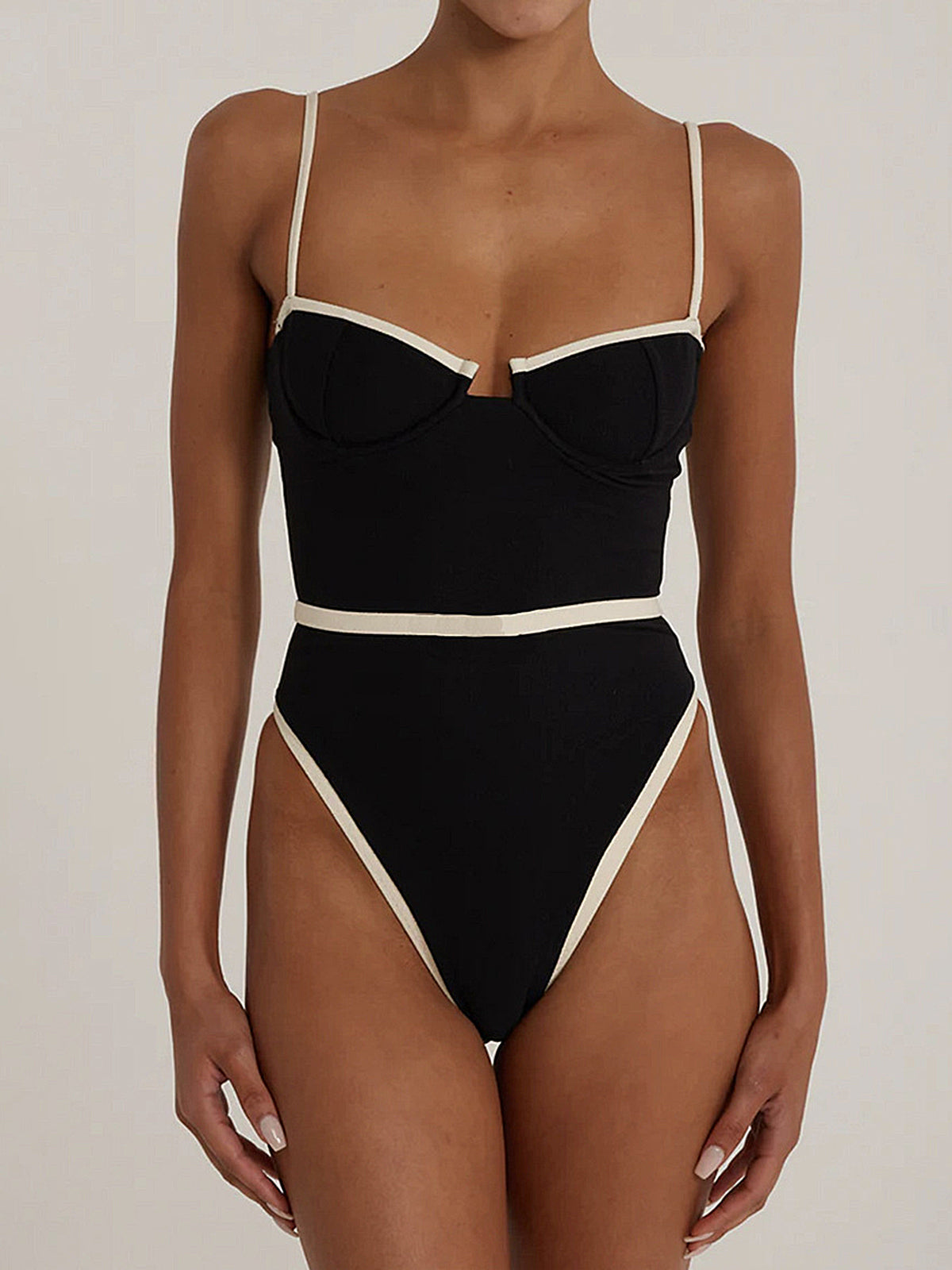 Front view of a woman wearing a black one-piece swimsuit with beige trim and thin straps.