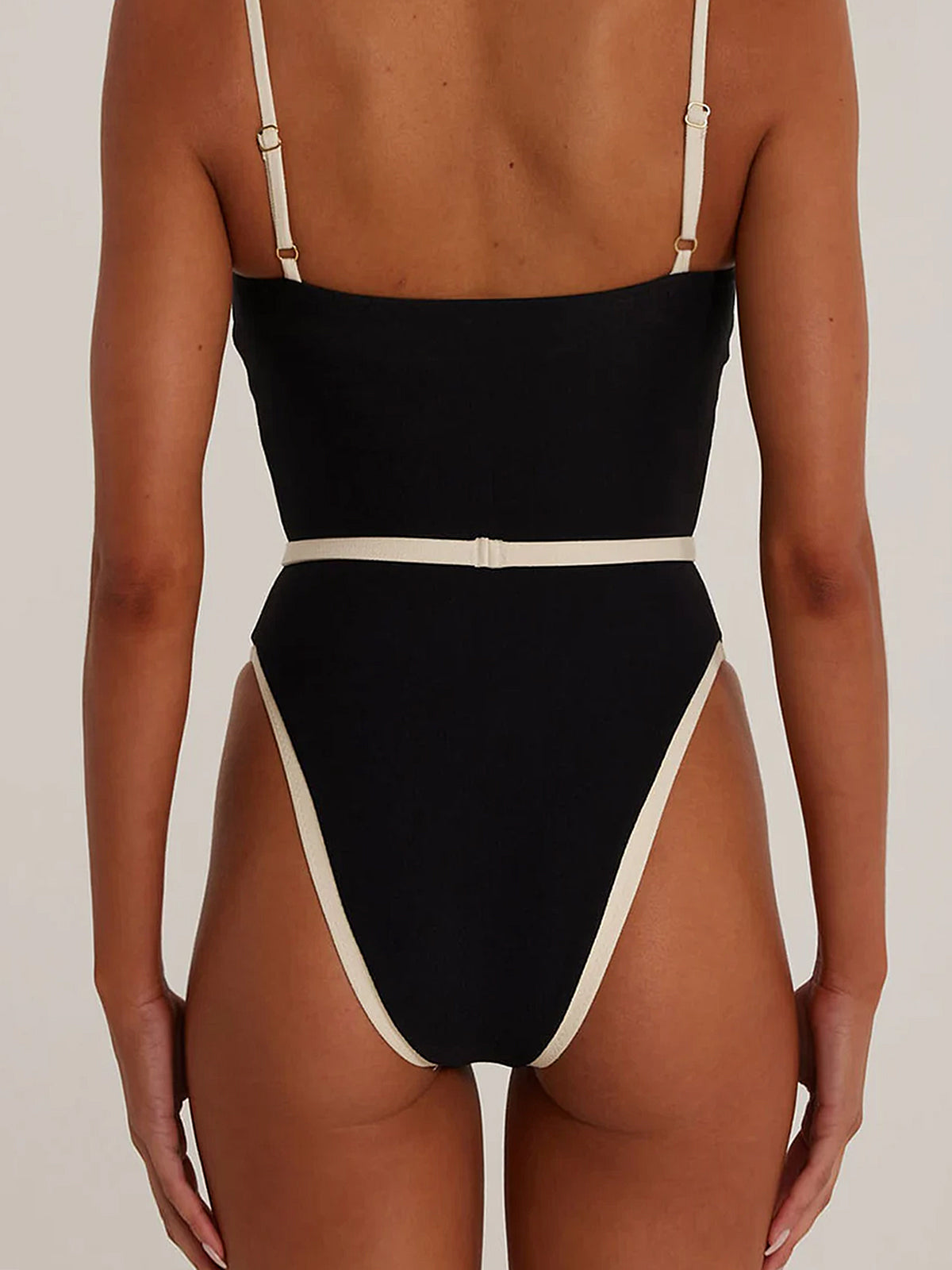 Back view of a woman wearing a black one-piece swimsuit with beige trim and a belt detail.