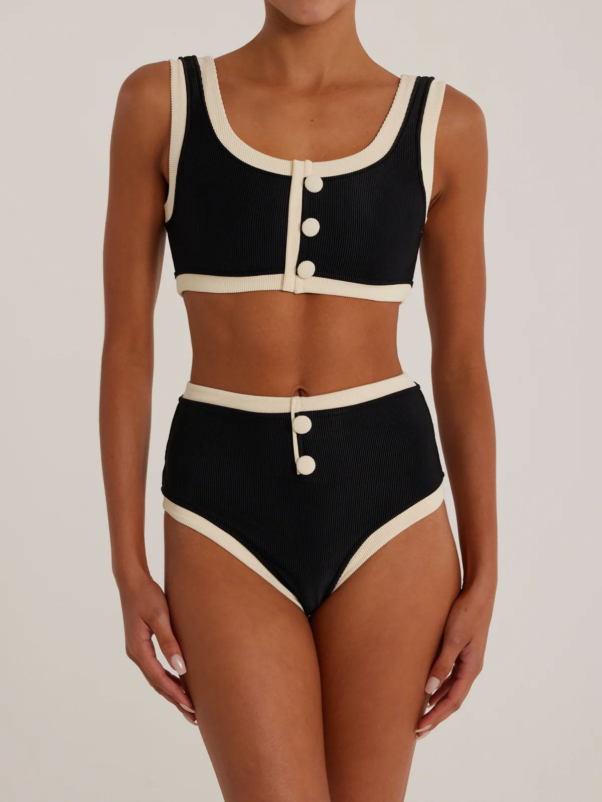 Woman wearing a black and cream ribbed bikini with high-waisted bottoms and a scoop neck top with button details
