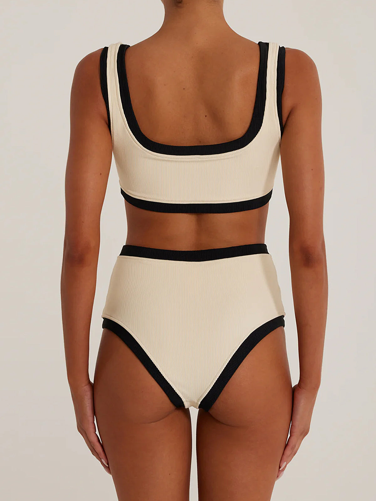 Back view of a woman wearing a cream and black ribbed bikini with high-waisted bottoms and a scoop neck top