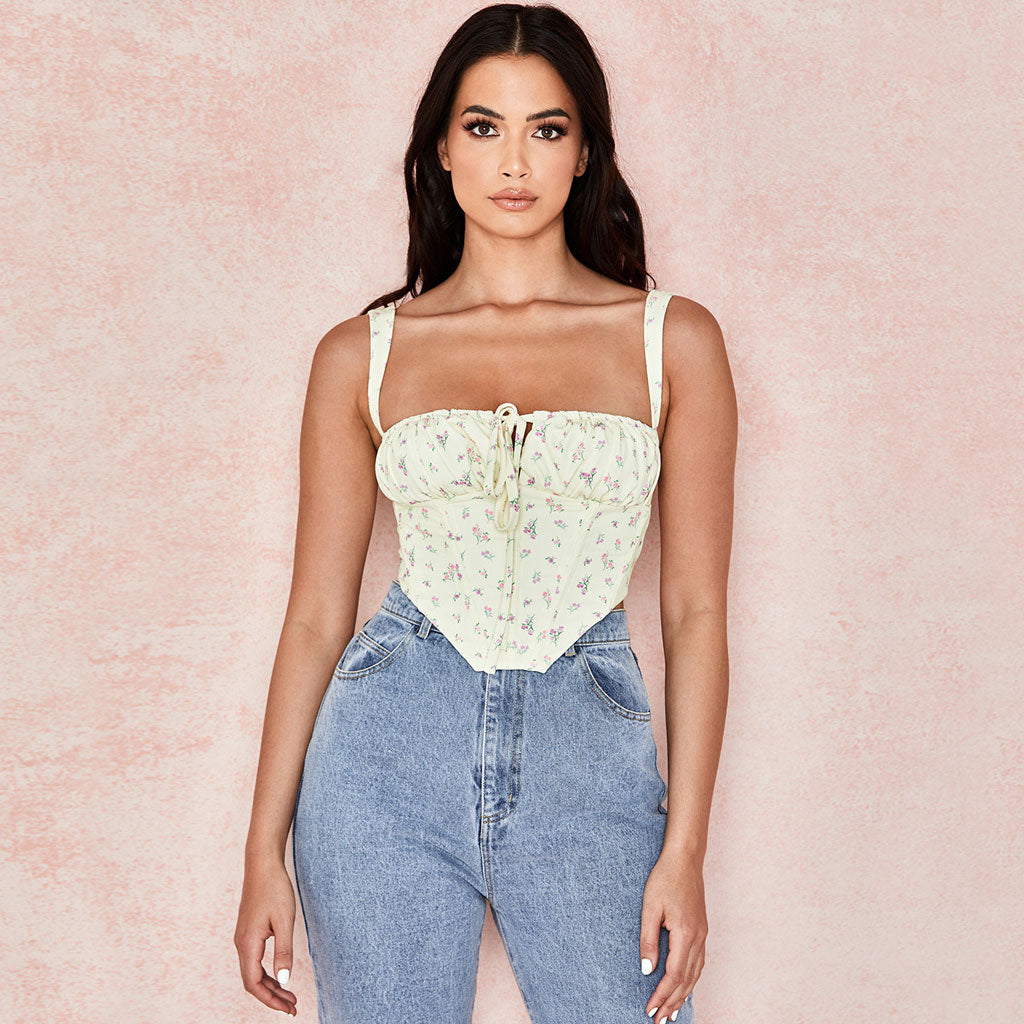 Woman in a yellow floral corset top and blue jeans posing against a pink background