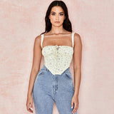 Woman in a yellow floral corset top and blue jeans posing against a pink background