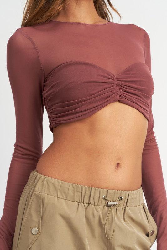 Close-up of a woman's torso wearing a rose long-sleeve mesh crop top with a ruched bust detail.