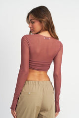 Back view of a woman wearing a rose long-sleeve mesh crop top and tan cargo pants.
