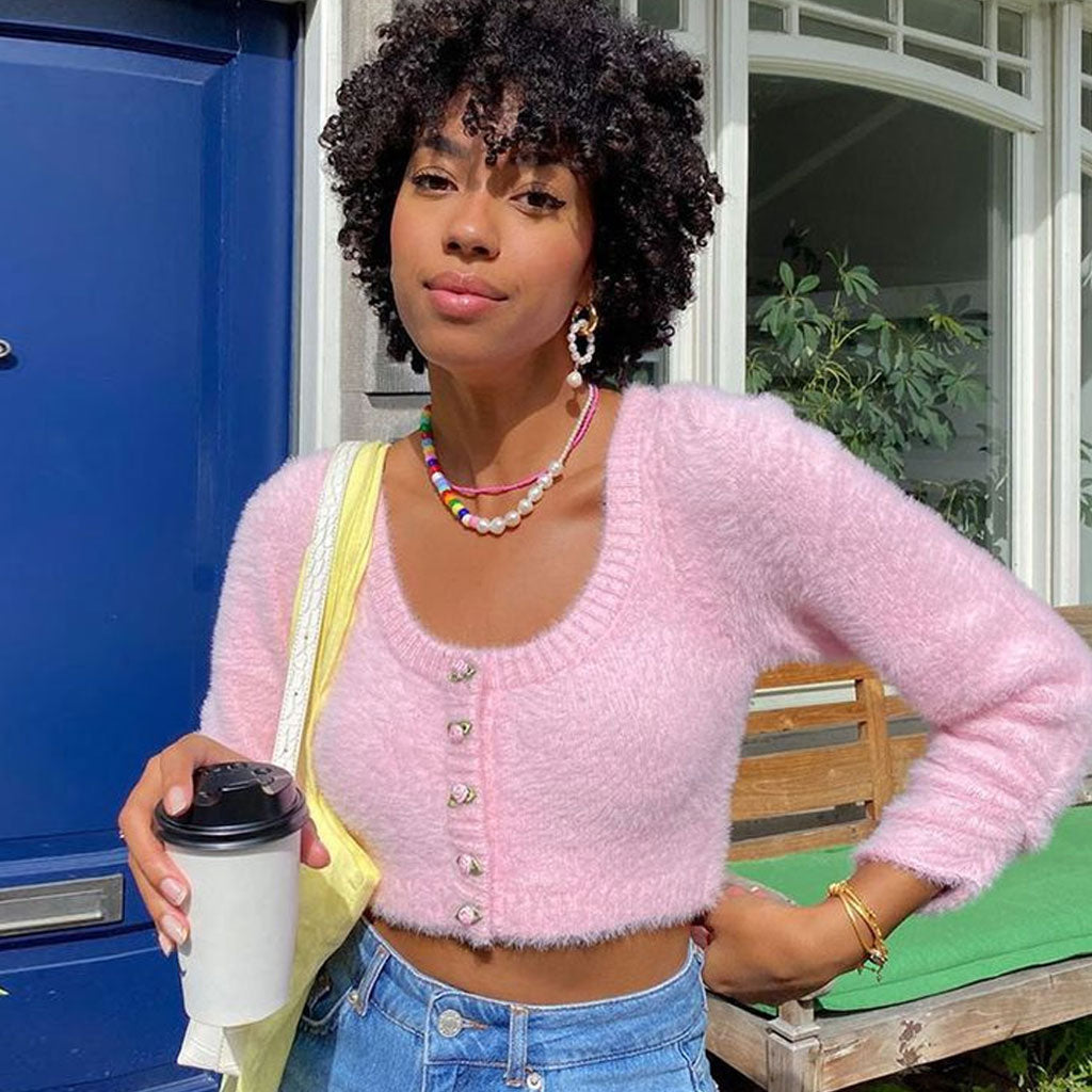 woman wearing a pink fuzzy cropped cardigan with jeans and a colorful necklace