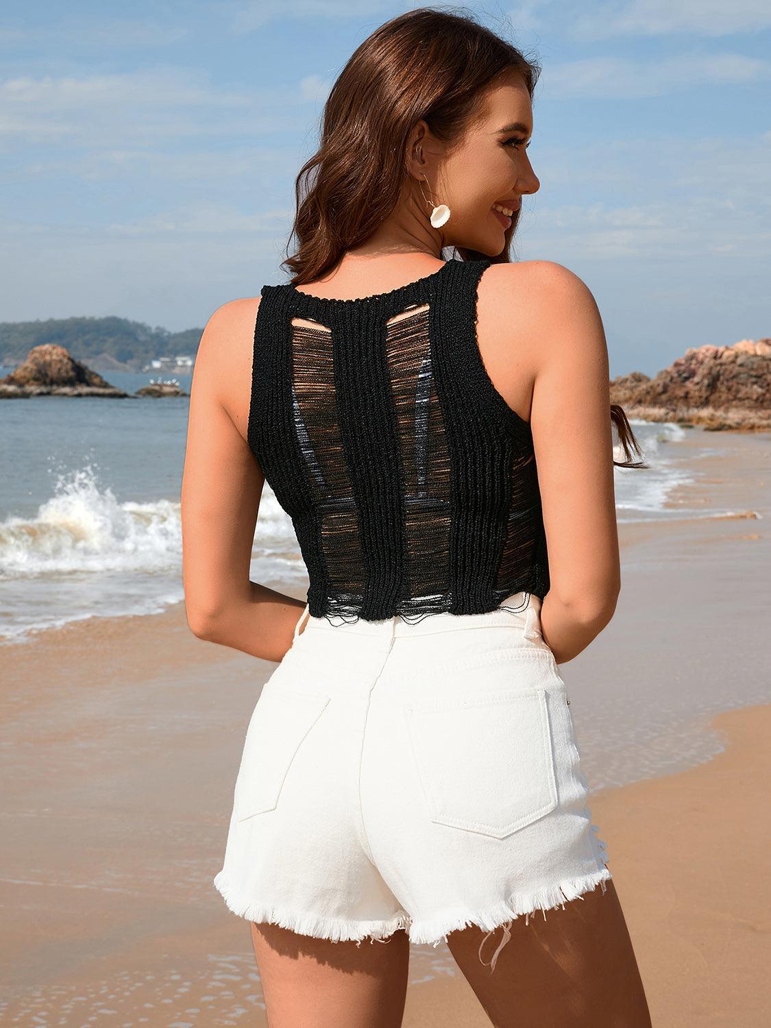 Back view of a woman wearing a black distressed knit crop top and white denim shorts on a beach
