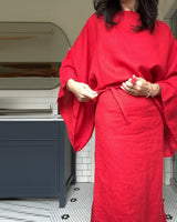 Close-up of a woman tying the belt of her red linen dress.