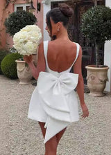 back view of a woman in a white mini dress with a large bow and pearl trim