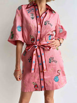 A woman in a pink shirt dress with colorful embroidered motifs and a matching belt, showing the front of the dress.