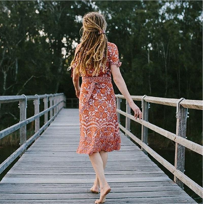 woman in orange floral wrap dress walking on a wooden bridge