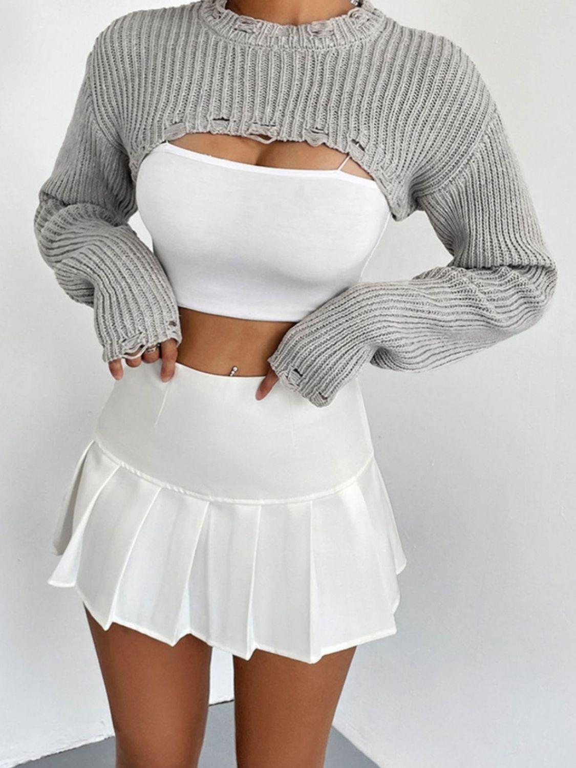 woman wearing a white crop top, a gray cropped sweater with cut-out details, and a white pleated mini skirt