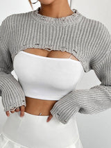 close-up of a woman wearing a white crop top and a gray cropped sweater with distressed details
