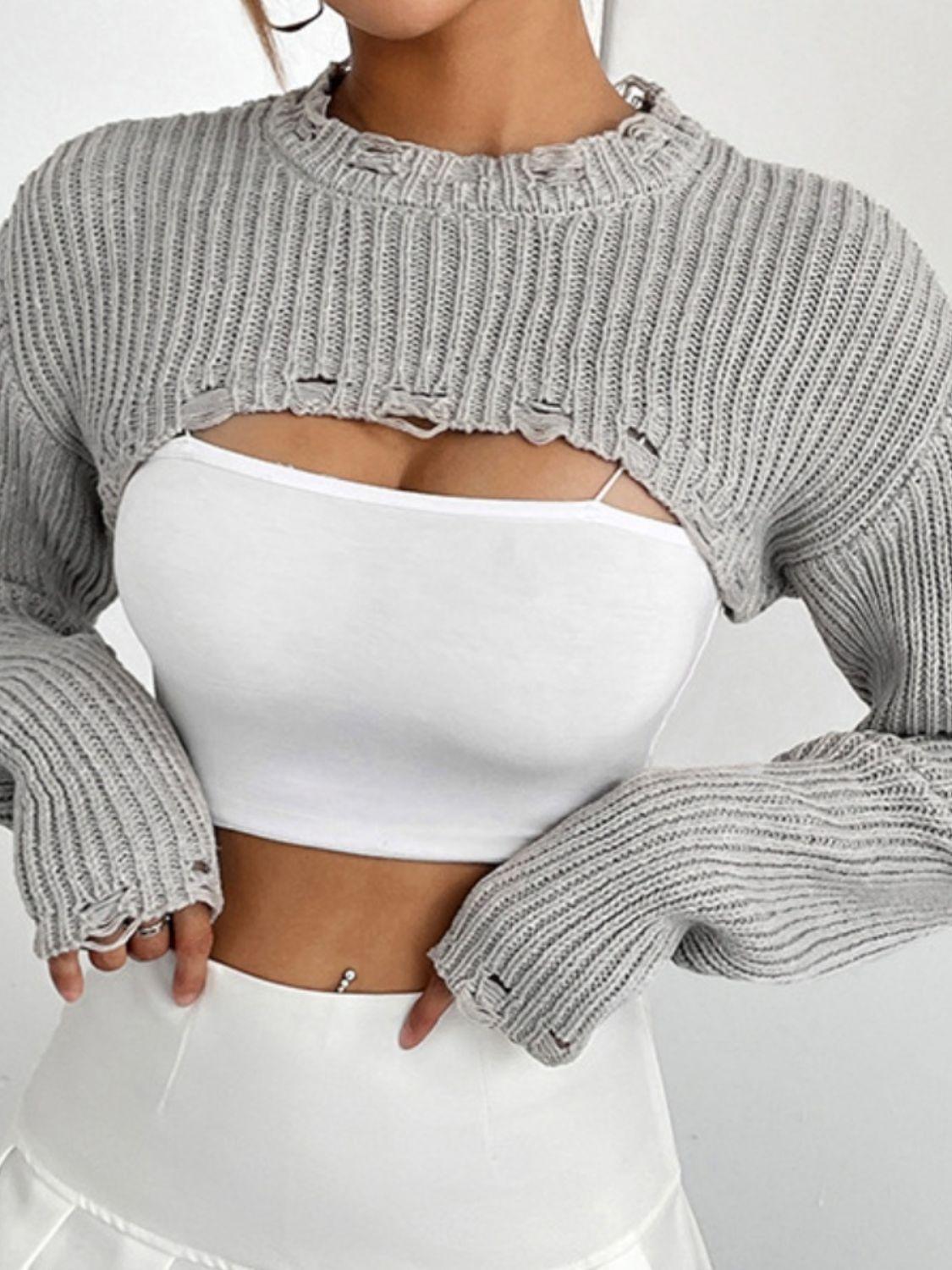 close-up of a woman wearing a white crop top and a gray cropped sweater with distressed details