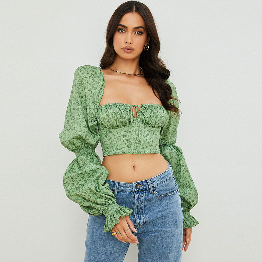 Woman wearing a green floral print crop top with puff sleeves and blue jeans, front view