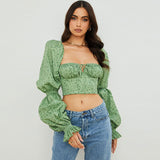 Woman wearing a green floral print crop top with puff sleeves and blue jeans, front view