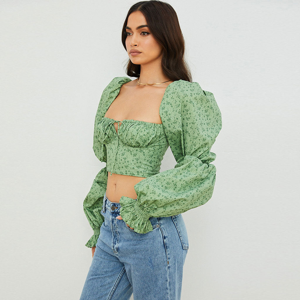 Woman wearing a green floral print crop top with puff sleeves and blue jeans, side view