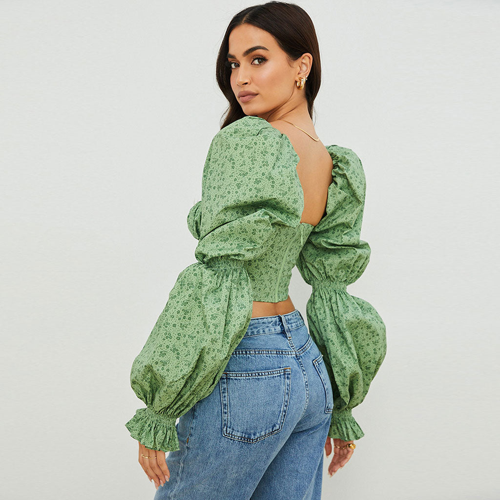 Woman wearing a green floral print crop top with puff sleeves and blue jeans, back view
