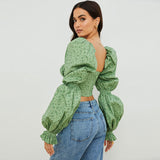 Woman wearing a green floral print crop top with puff sleeves and blue jeans, back view
