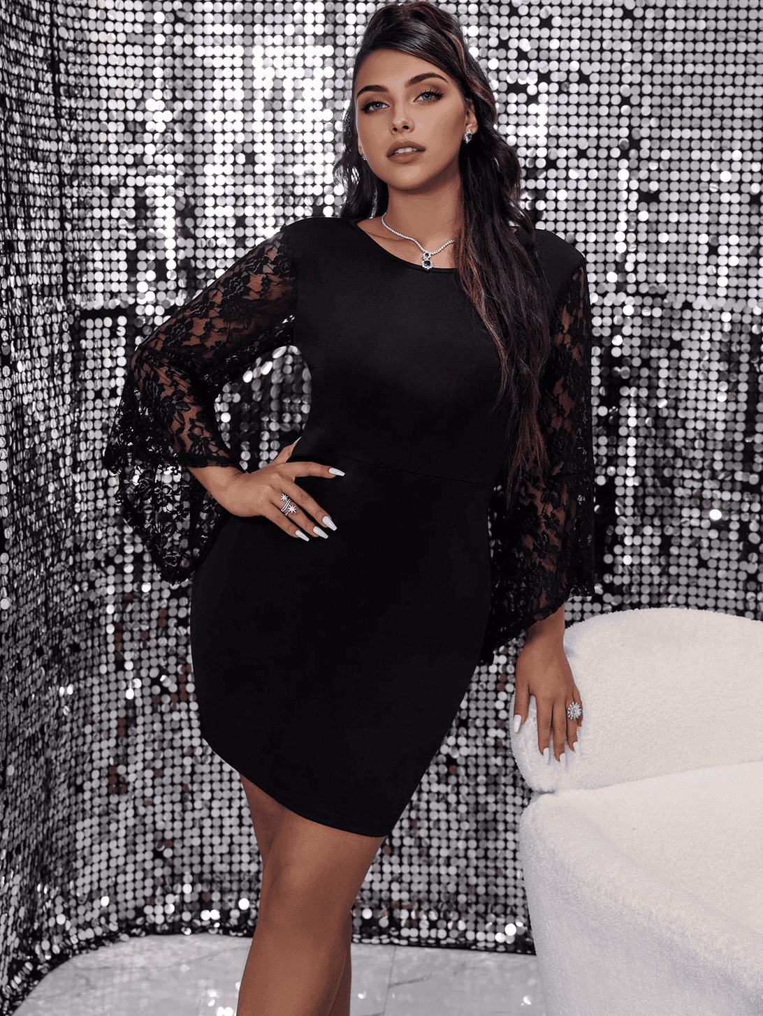 A woman in a black dress with lace sleeves and a sequined background.