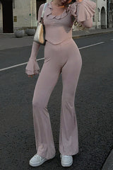 Woman wearing a pink long-sleeved top with flared sleeves and matching flare pants, standing on a street.