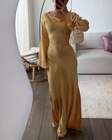 Woman in a gold satin dress with long bell sleeves, posing in front of a mirror.