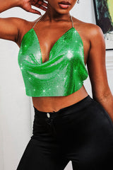 Woman wearing a green metallic mesh halter top with a plunging neckline and black pants, angled front view.