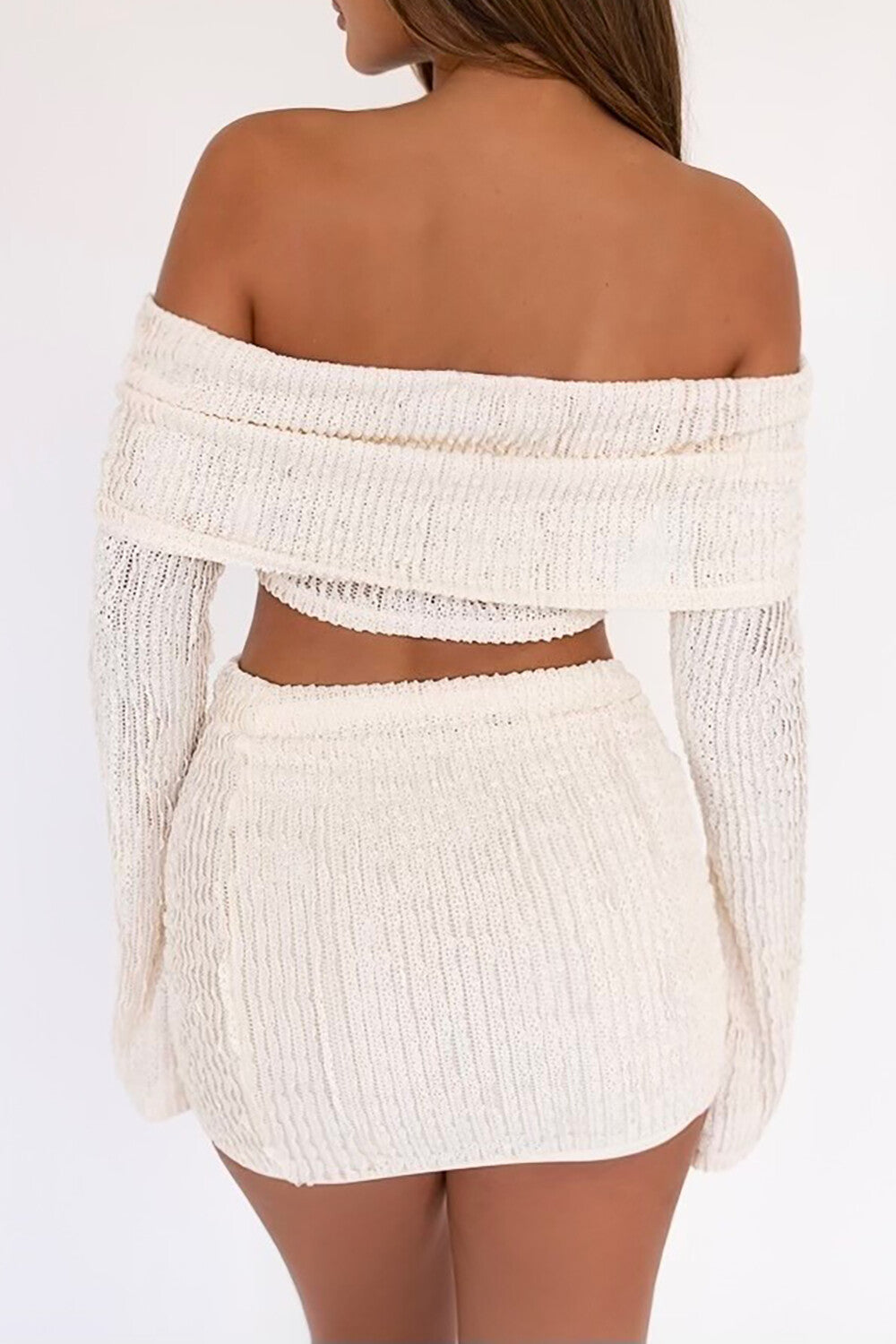 Back view of a woman in a white off-the-shoulder crop top and ruched mini skirt set.