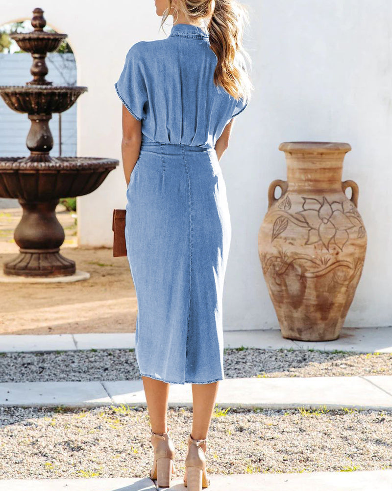 Back view of a woman in a light blue denim midi dress with short sleeves and a tie waist.